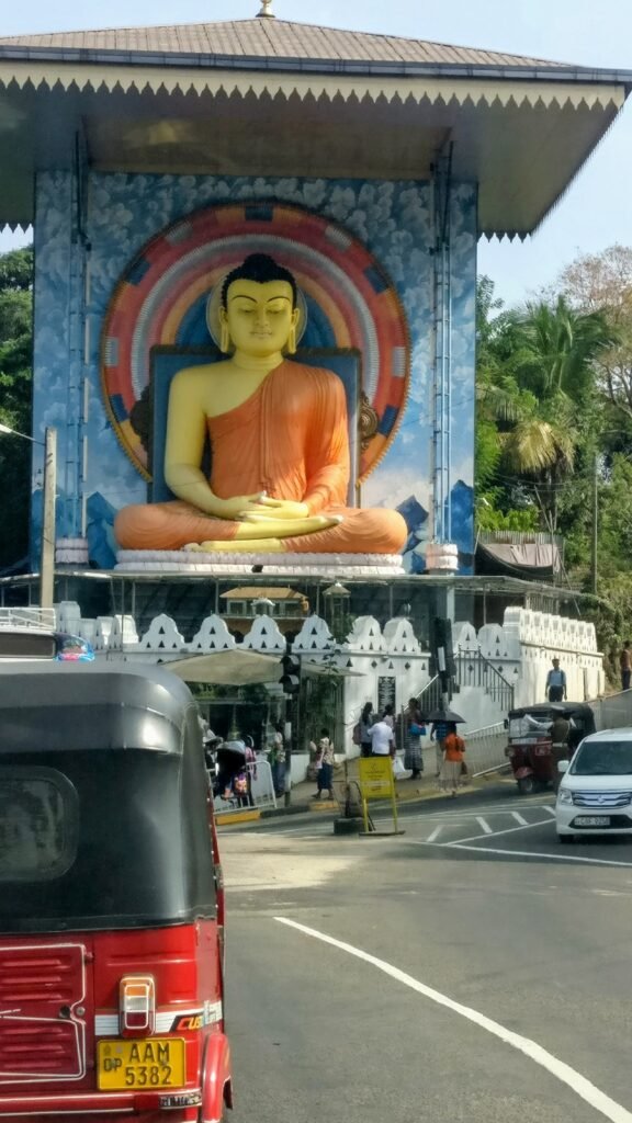 Reisekonzept Gold: Kandy Straßenszene mit großer Buddha Statue