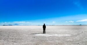 Mann der alleine auf einem weiten Salzsee steht und in die Ferne schaut. Er dreht uns den Rücken zu.