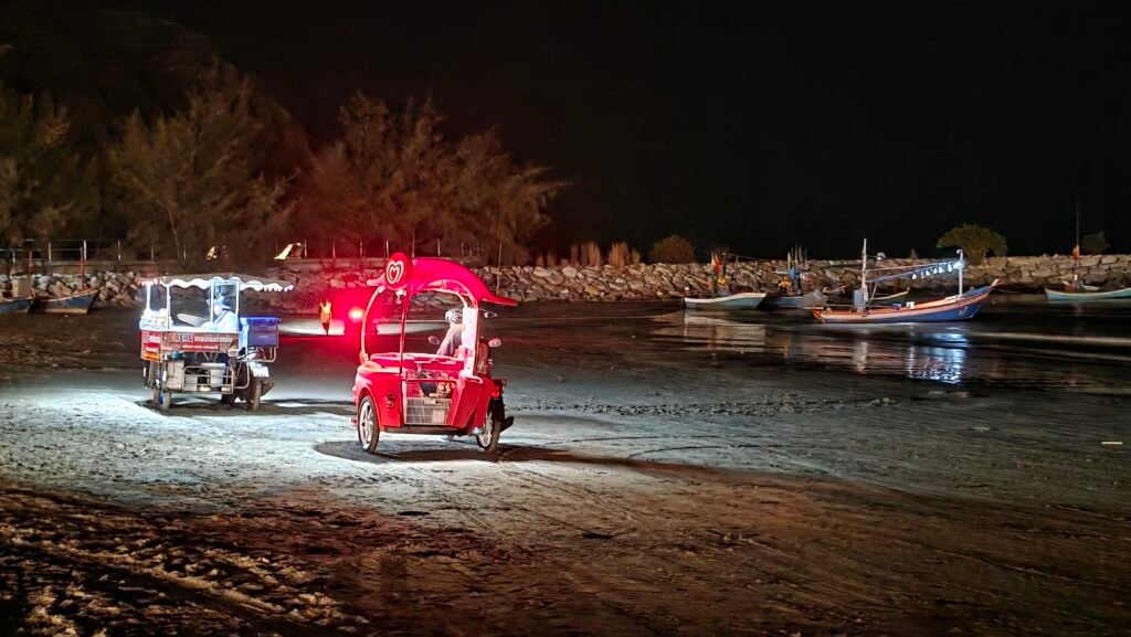 Verkaufs Tuk-Tuks am Strand mit Fischerbooten im Hintergrund